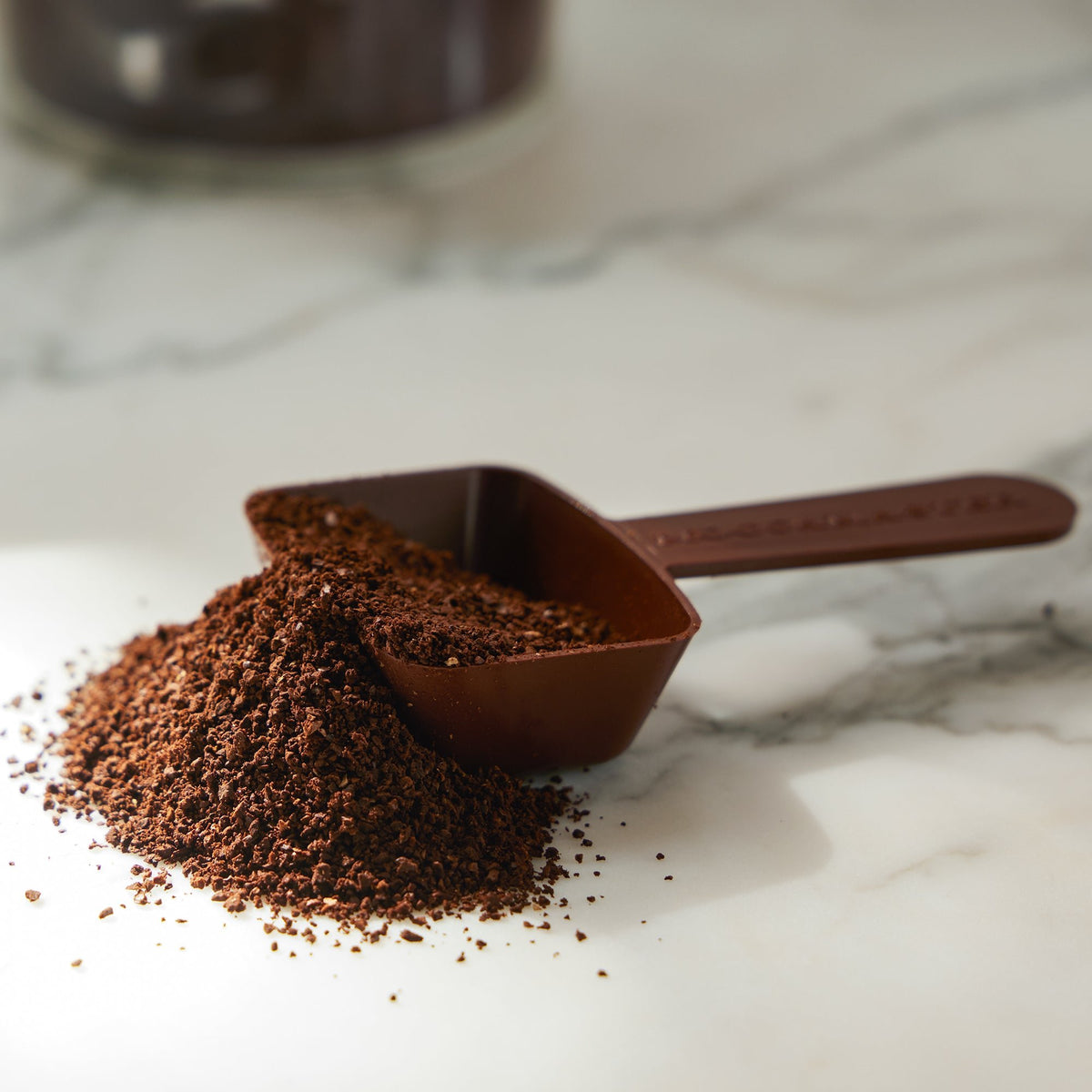 A 2-tablespoon brown coffee scoop overflowing with coffee grounds.