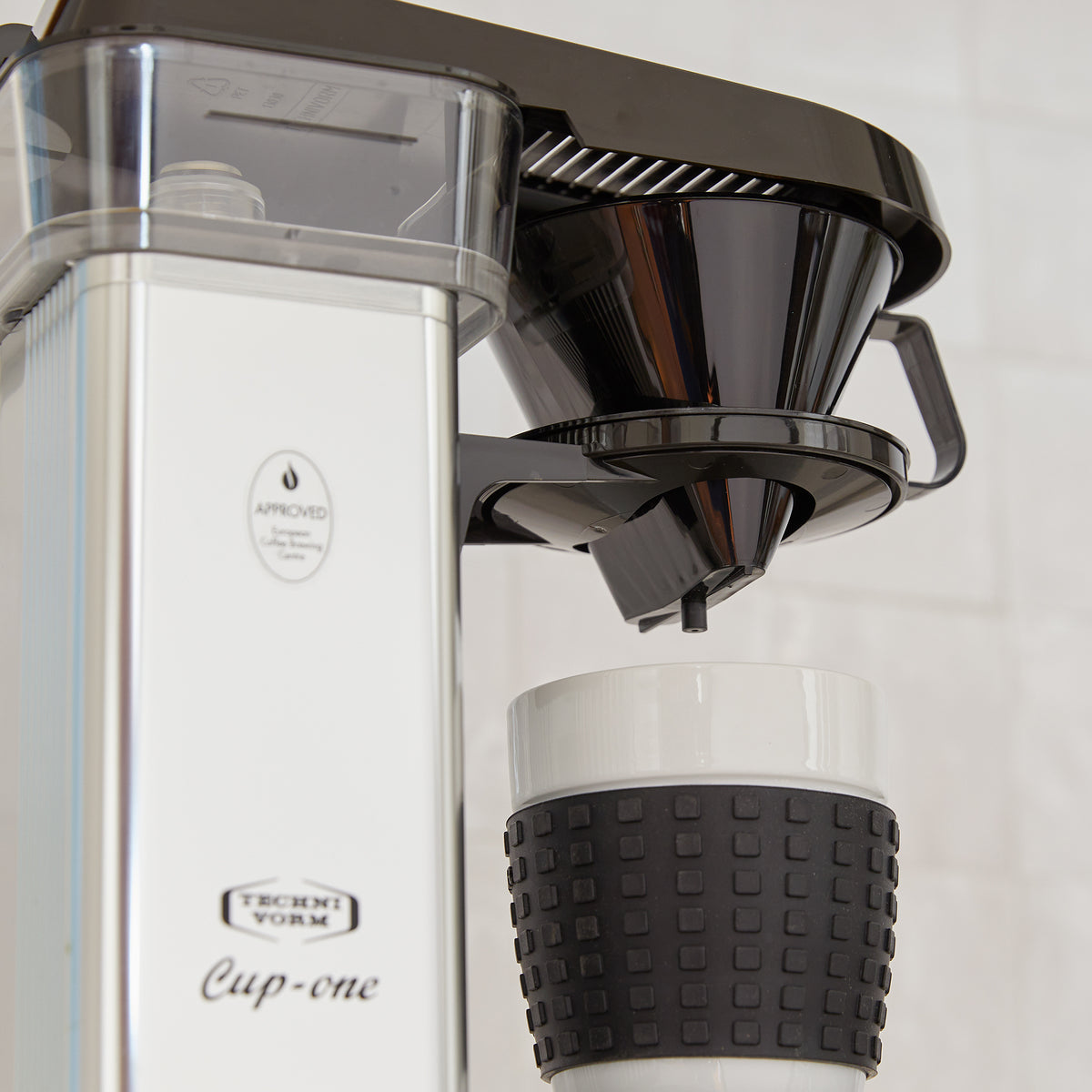 A close-up of the cup-one, focused on the drip brew basket and vented cover for the brew basket and water reservoir. The 'Approved by European Coffee Brewing Centre' sticker is visble, and the Technivorm Cup-one badging.