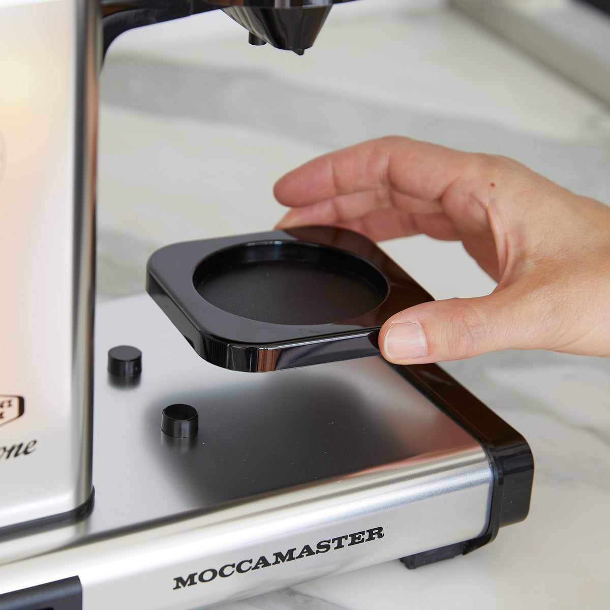 A hand removing the cup holder from a Moccamaster Cup-One coffee brewer.