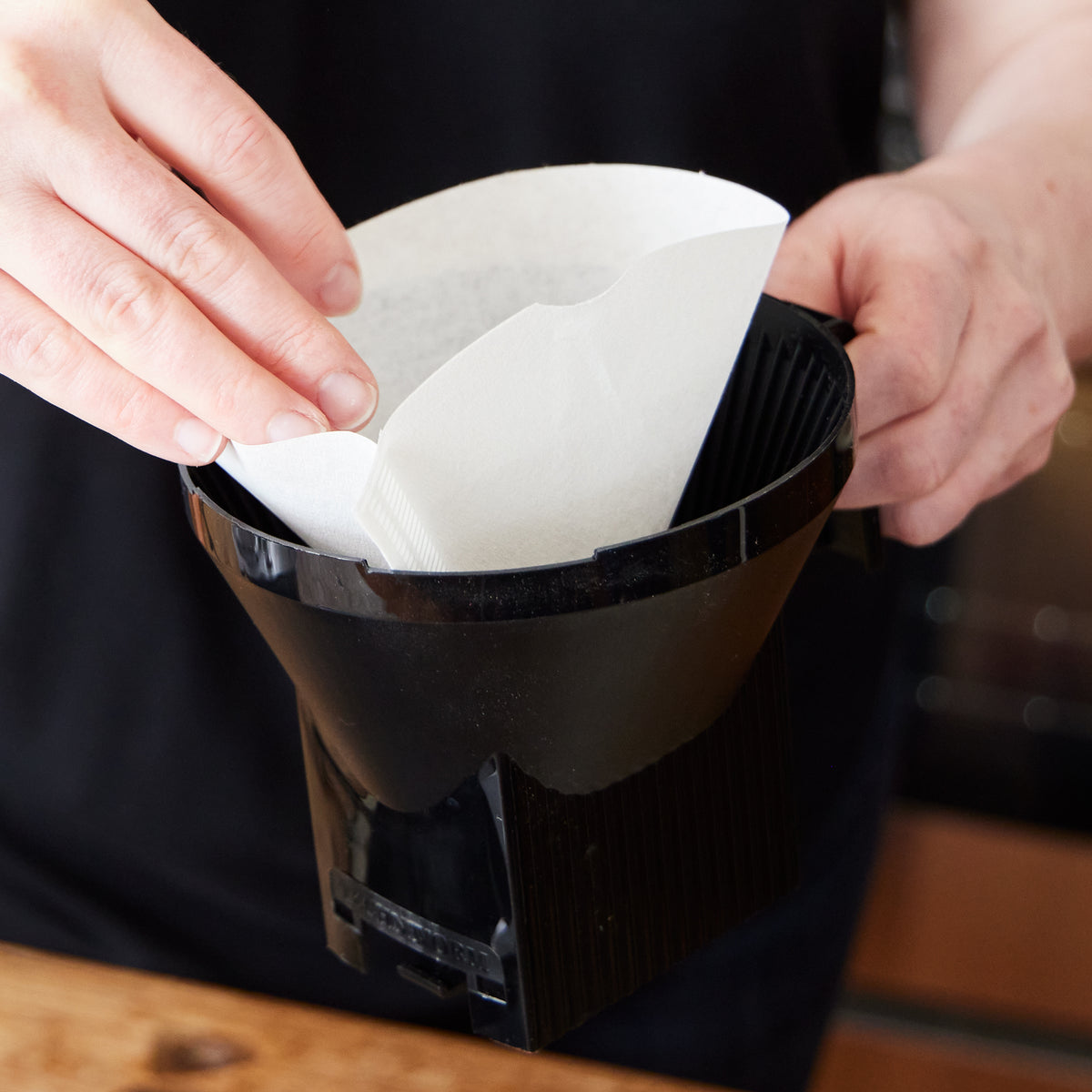 Close up of someone inserting a white paper filter into a Moccamaster brew basket.