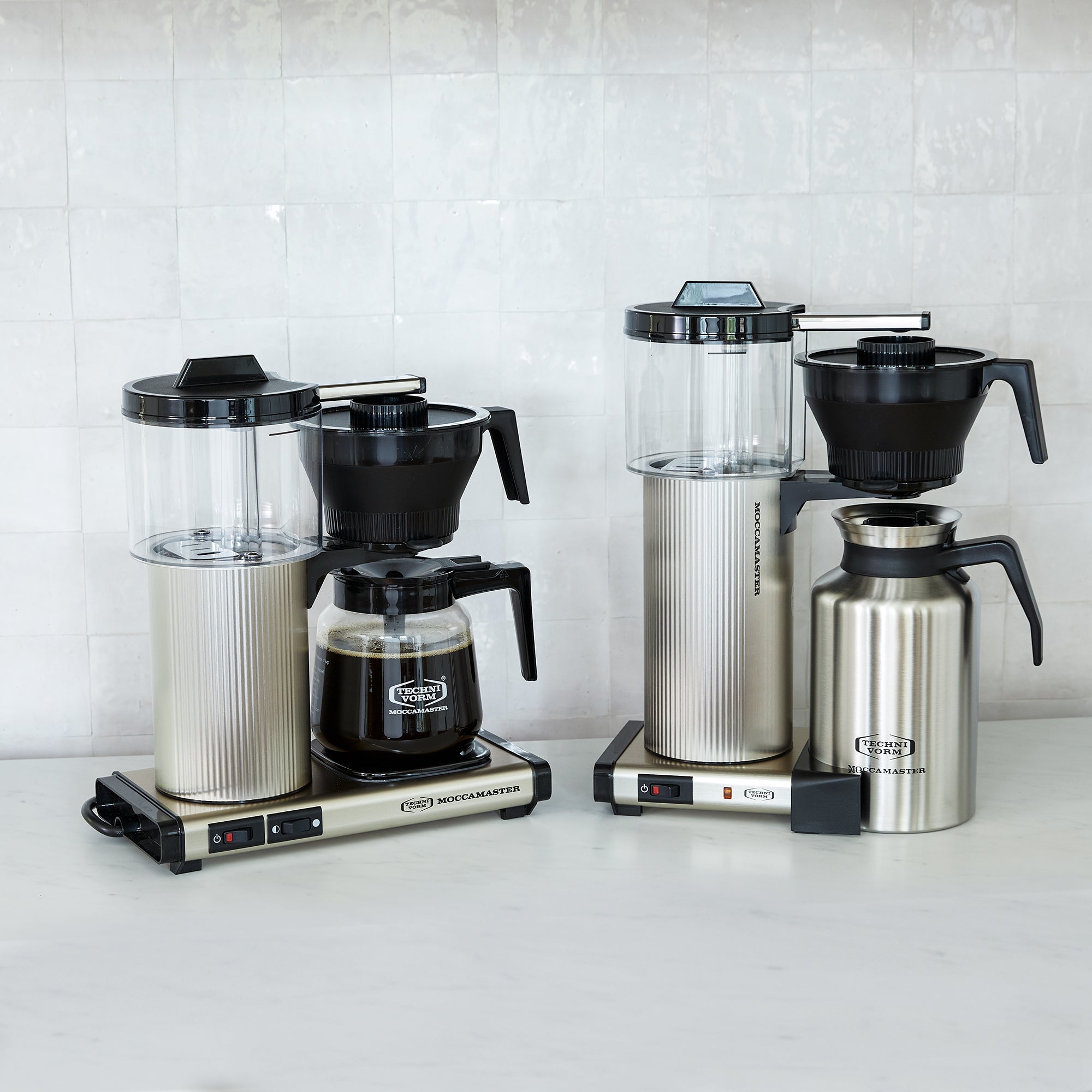 Moccamaster coffee machine with silver body, clear water reservoir, and black glass carafe filled with coffee