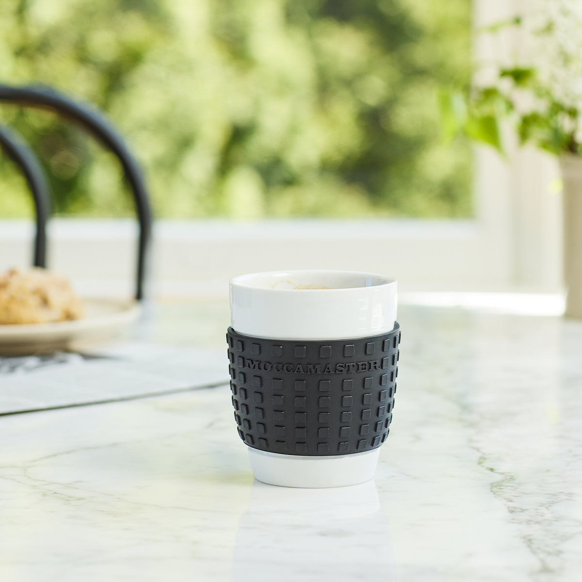 A porcelain Cup-One mug with black silicone sleeve sitting on a marble table.