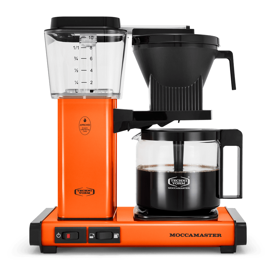 Front shot showing Moccamaster KBGV Select in Orange, with rectangular tower and base, clear acrylic water reservoir with fill level marks, power and volume selector switch, glass carafe with black handle, and black automatic brew basket.